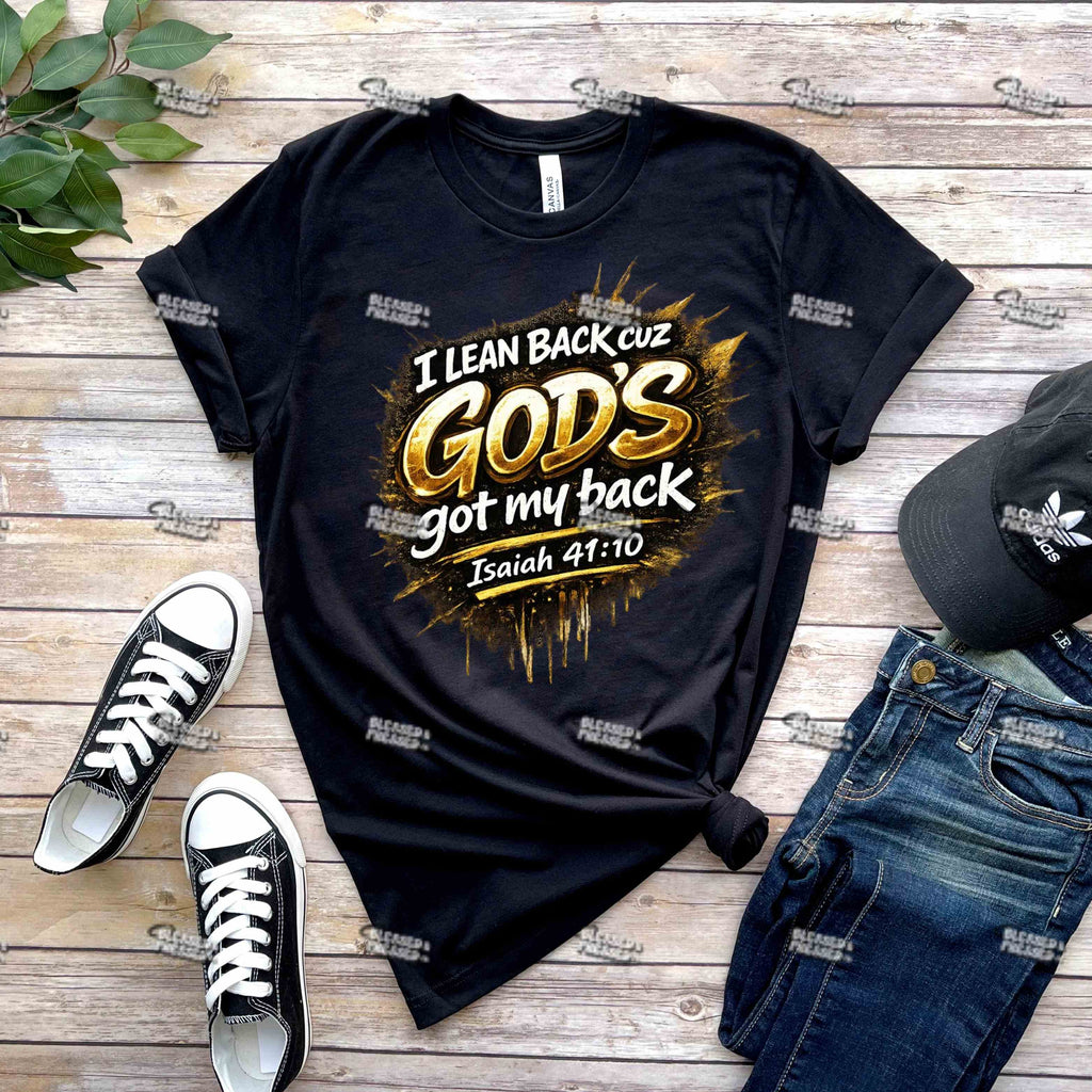Black t-shirt with 'I Lean Back cuz God's got my back' text, paired with black sneakers and jeans on a wooden surface.