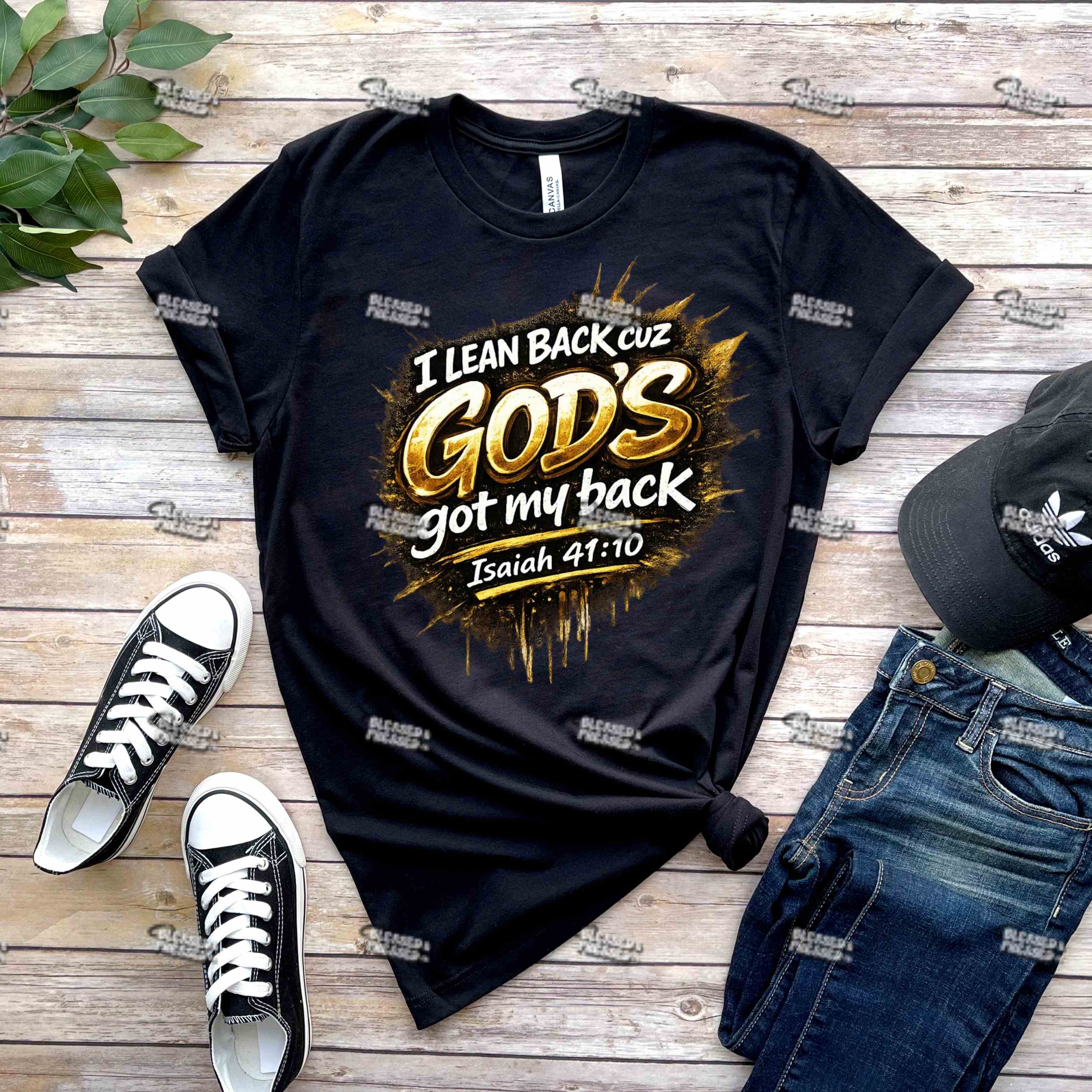 Black t-shirt with 'I Lean Back cuz God's got my back' text, paired with black sneakers and jeans on a wooden surface.